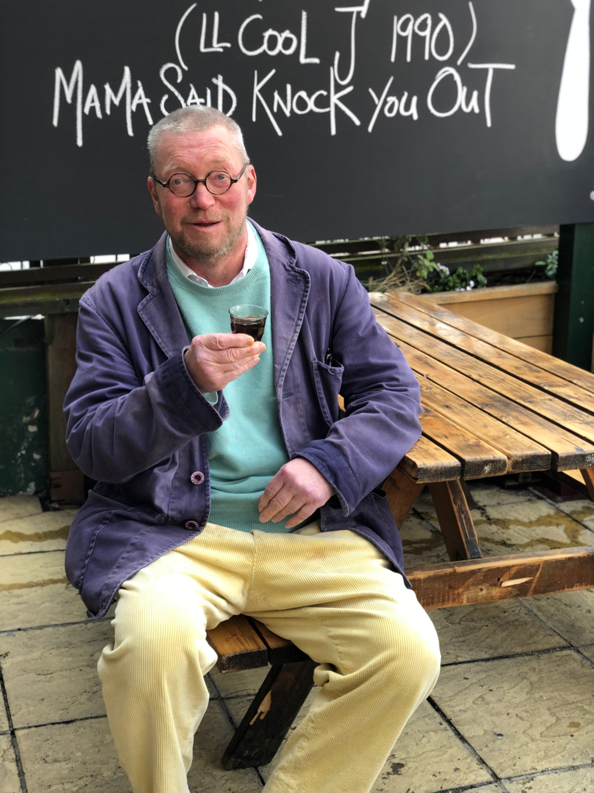 Man sitting on a wooden bench holding a glass of red wine, with text in the background.